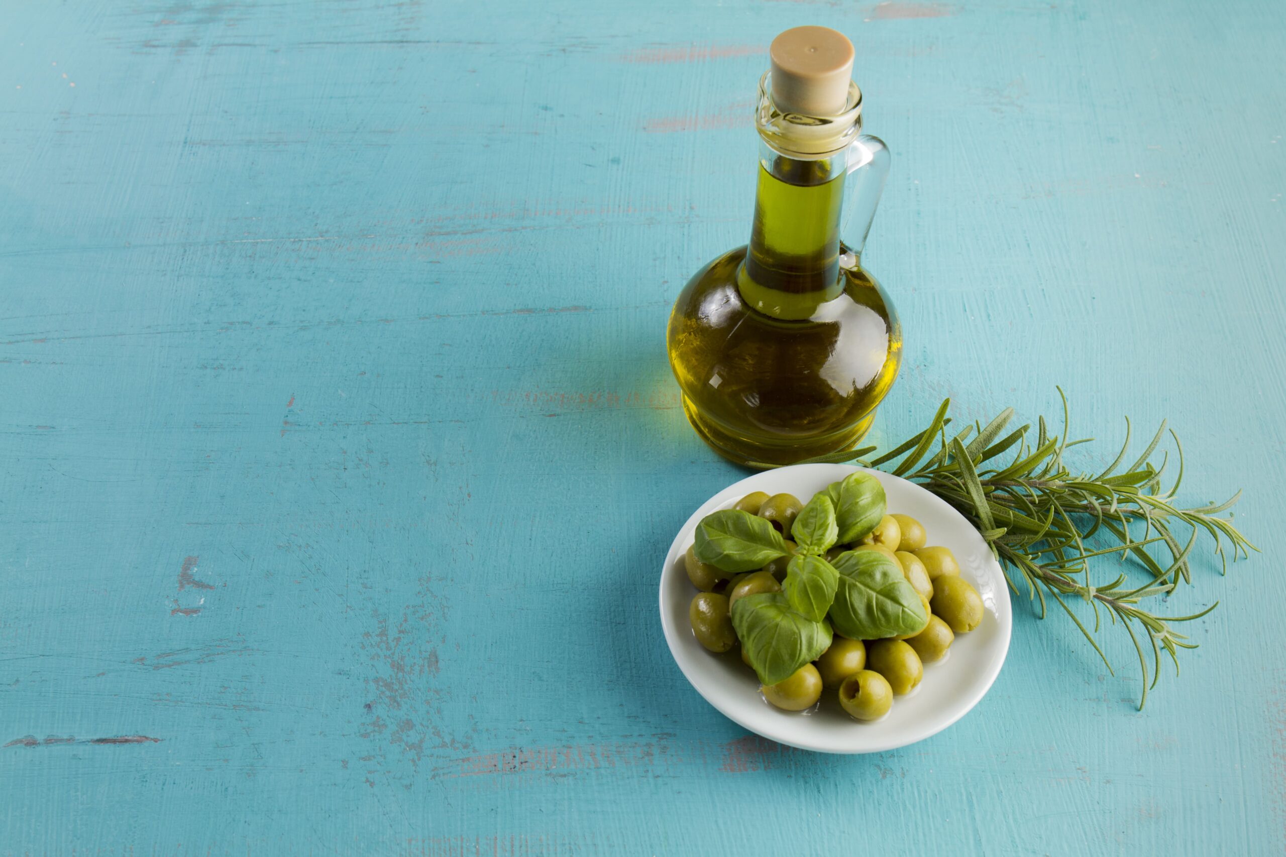 botella de aceite verde junto a cuenco de aceitunas sobre mesa rústica azul